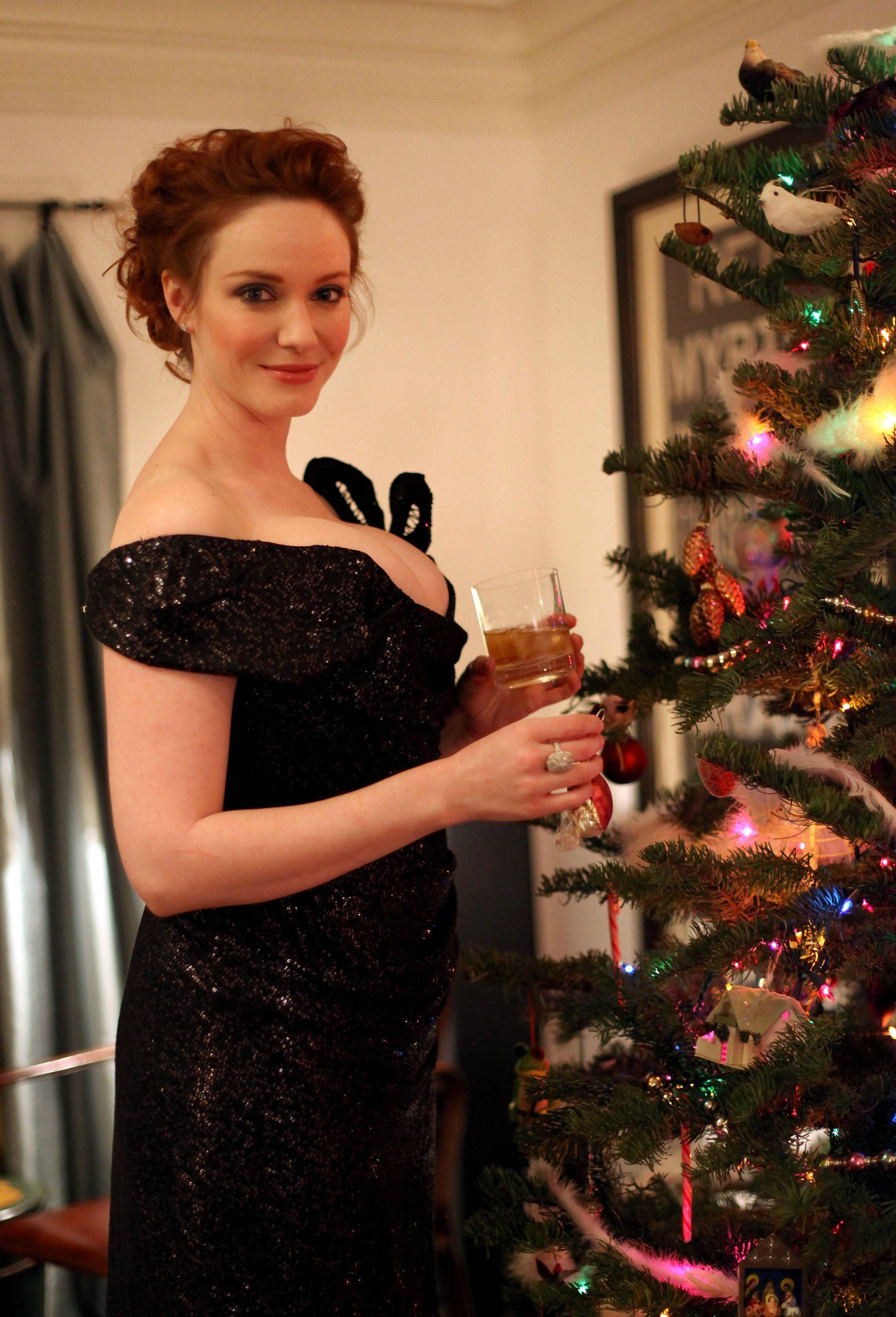 Mommy Christina in a shoulderless black dress, smiling at you as she decorates a Christmas tree.