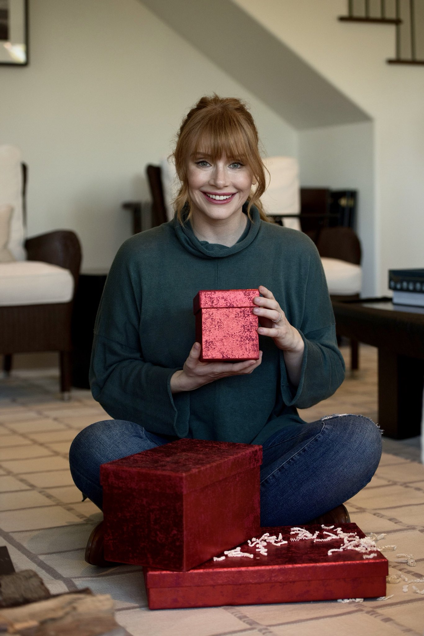 Auntie Bryce sitting cross-legged on the floor, holding a boxed gift with a pile of gifts in front of her.