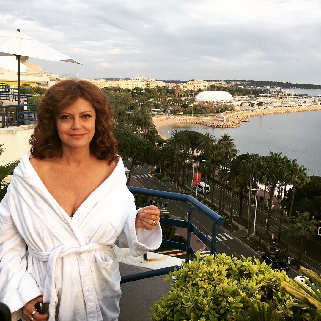 Mommy Susan in a white bathrobe, standing on a balcony overlooking the Cannes coast.