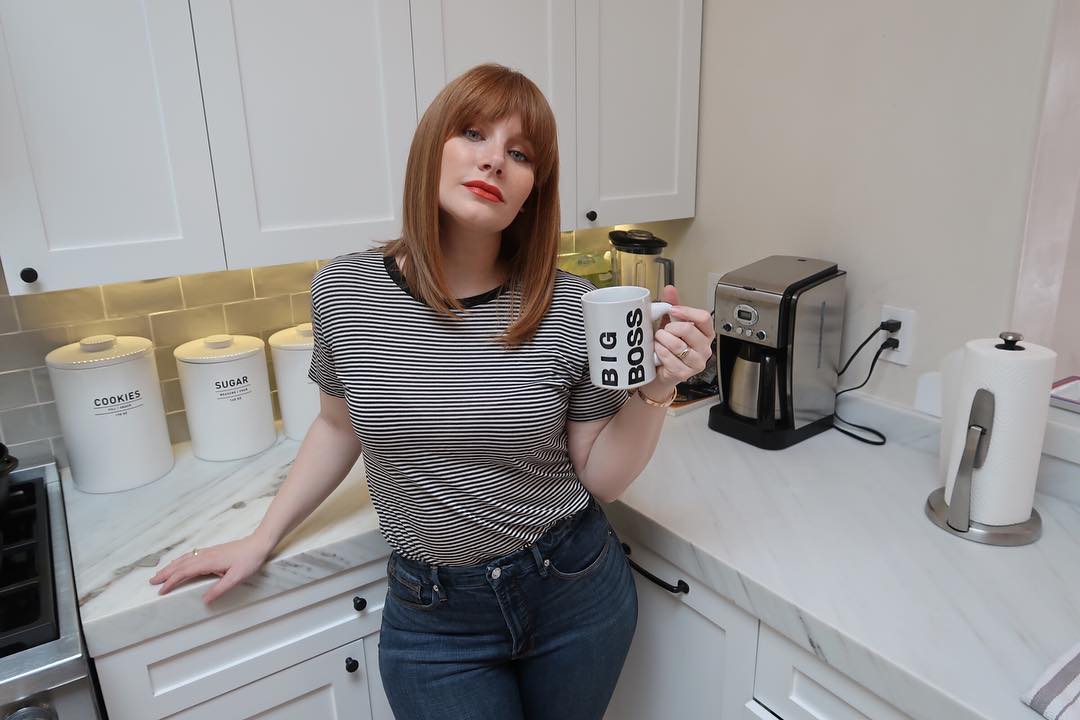 Mommy Bryce in jeans and a tight, striped top, leaning against the kitchen counter with a cup of coffee.