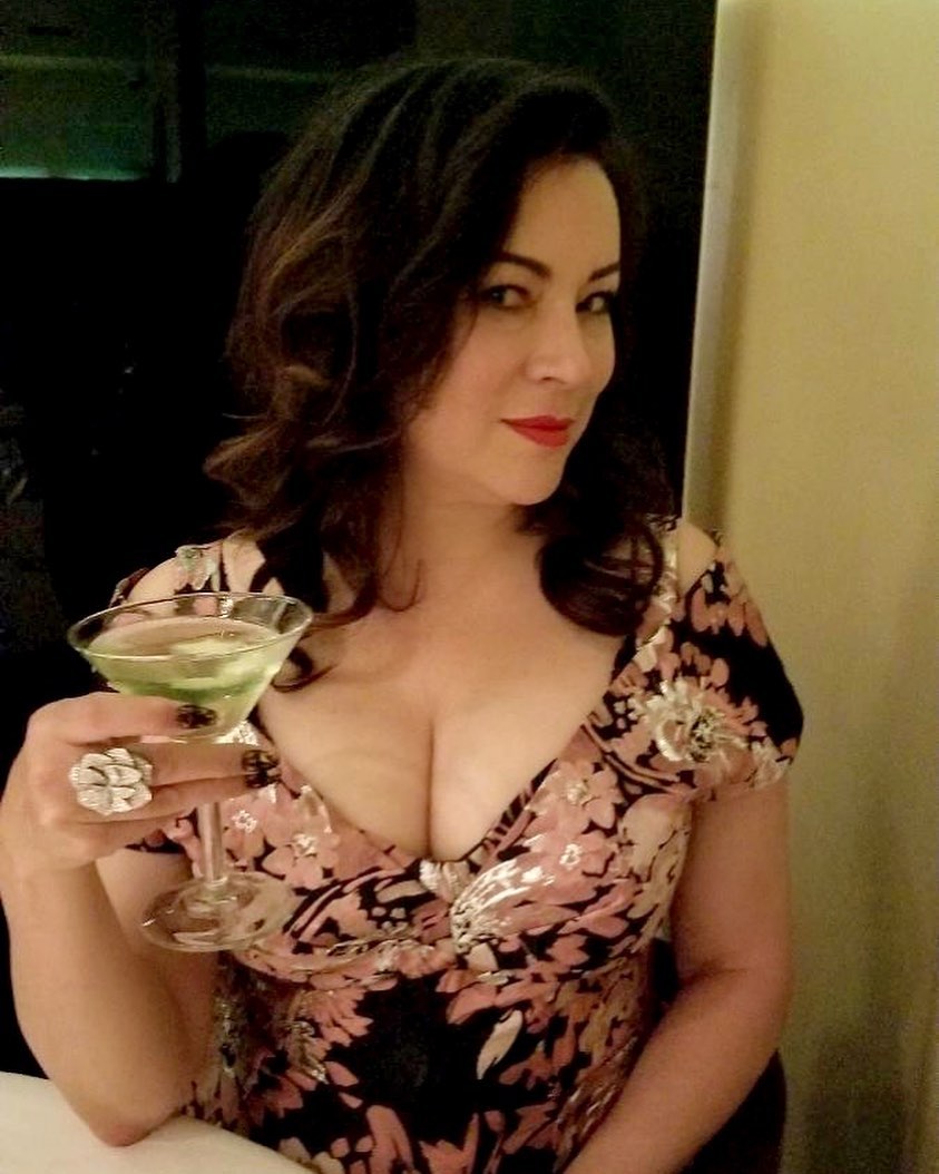 Mommy Jennifer sitting across from you at a dinner table with a drink in hand, her floral dress displaying her bountiful cleavage.